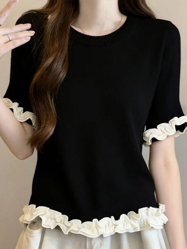 A woman wearing a black short-sleeve knit top with cream ruffled trim at the sleeve cuffs and hem, paired with a light cream skirt. The photo is cropped from the neck down against a plain beige background.