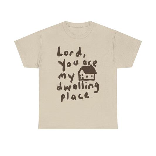 A light beige crewneck t-shirt with a dark brown graphic print that reads 'Lord, You are my dwelling place.' next to a small house illustration, shown on a plain white background.